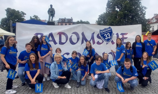 Uczniowie w niebieskich koszulkach stojący przed banerem z napisem Radomskie Dni Godności