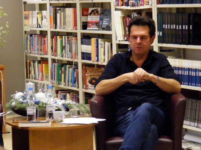 Marcin Kępa siedzący przy stoliku, wśród książek