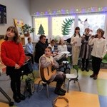 Uczniowie i Ksiądz grający na instrumentach muzycznych i śpiewający kolędy, tablica multimedialna z tekstami kolęd