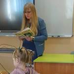 Kobieta czyta dzieciom książkę.W tle  monitor multimedialny i biała tablica