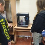 >Uczniowie wpatrzeni w drukarkę 3D