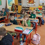 Uczniowie siedzący przy stolikach w klasie, ubrani na zielono