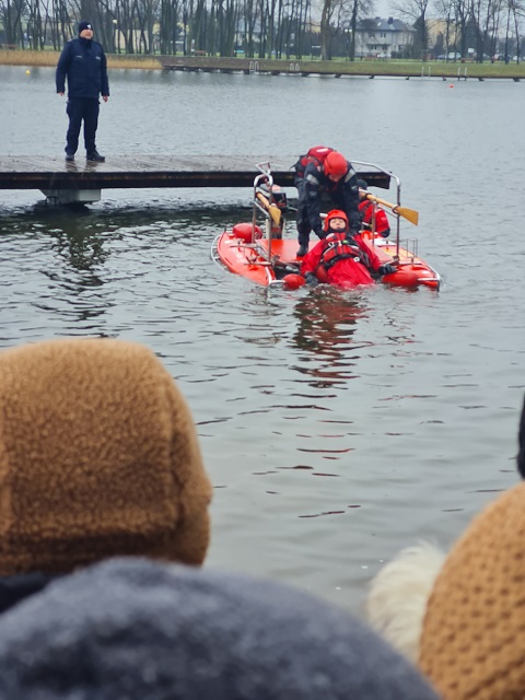 Na kładce nad wodą stoi policjant a w wodzie ktoś jest i ratownicy przy nim