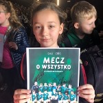Dziewczynka trzyma zdjęcie drużyny, a na nim jest napis Mecz o wszystko