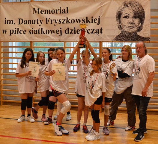 Dziewczynki z drużyny sportowej z PSP 33 wraz z trenerem, nad nimi baner z nazwą Memoriału